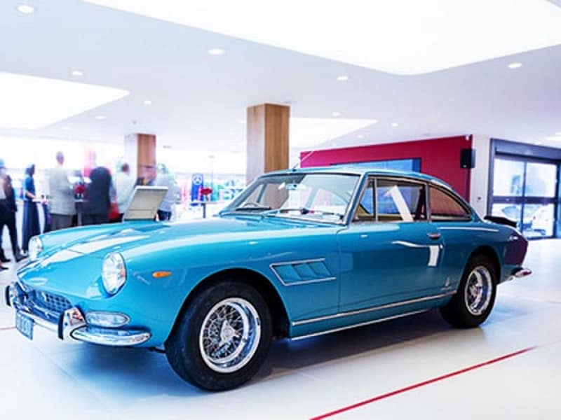 Classic blue Ferrari coupe on display in a modern showroom.